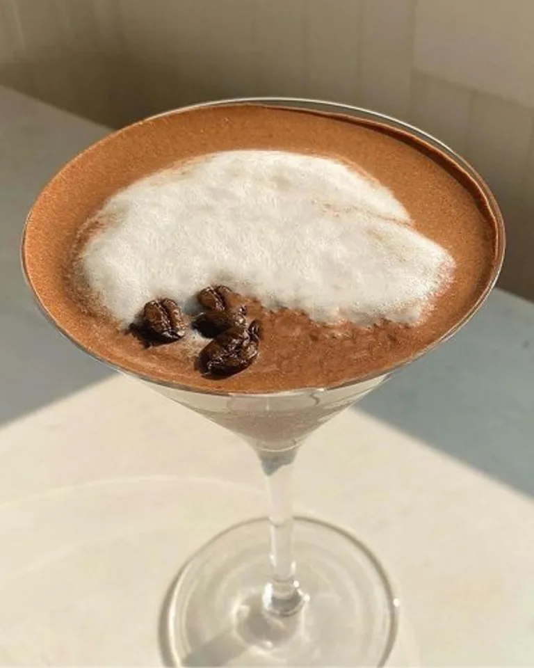 Espresso martini with white foam and espresso bean garnish on top.