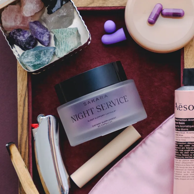 Sakara Life Night Service jar on a tray with crystals, ear plugs, Aesop hand cream, and palo santo with a lighter