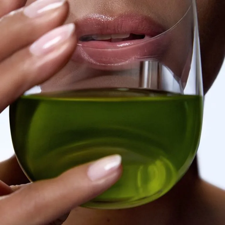 A close-up of a female taking a sip out of a drinking glass with a green liquid inside, which contains Sakara's Daily Elixir Liquid Multivitamin