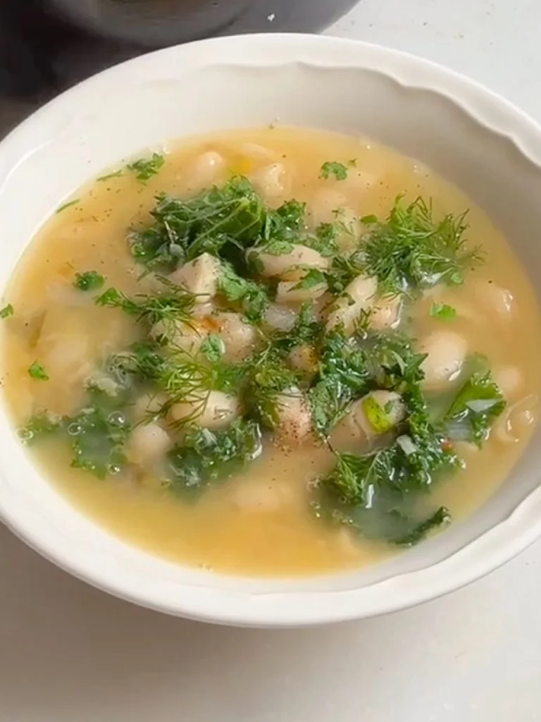 Bowl of vegetable soup topped with fresh herbs and chopped greens.