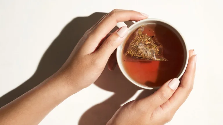 An overhead shot of hands holding a cup of tea with a tea bag seeping.
