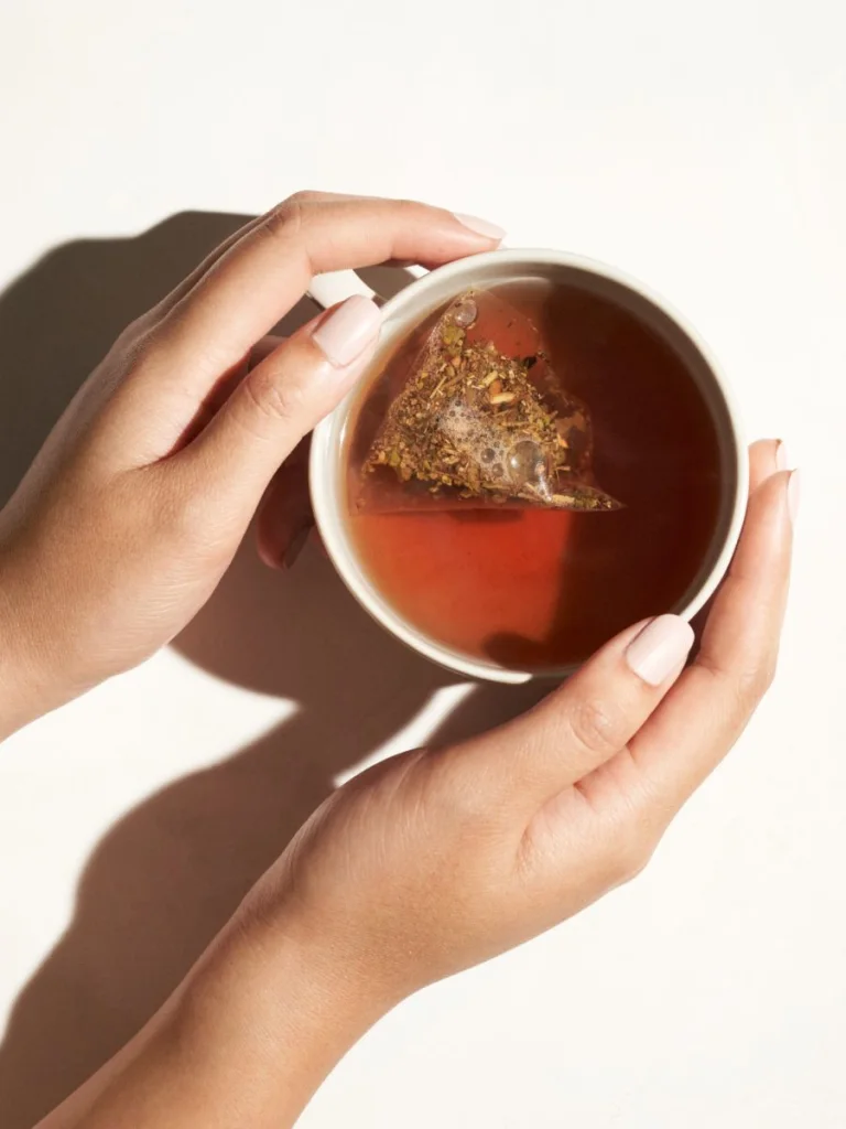 An overhead shot of hands holding a cup of tea with a tea bag seeping.