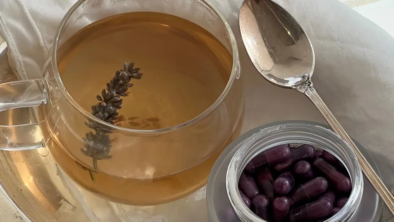 A clear glass mug with tea and a lavender stem next to Sakara Night Service capsules in a frosted jar.
