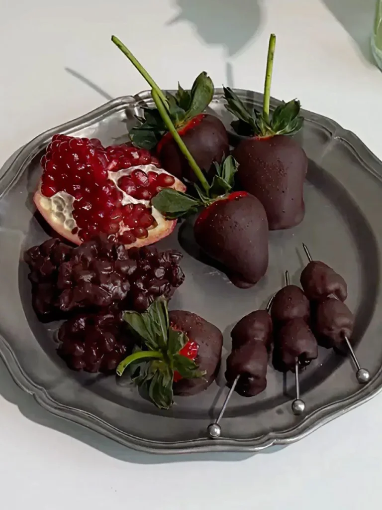 Silver platter with dark chocolate covered strawberries, raspberries, and pomegranate seeds.