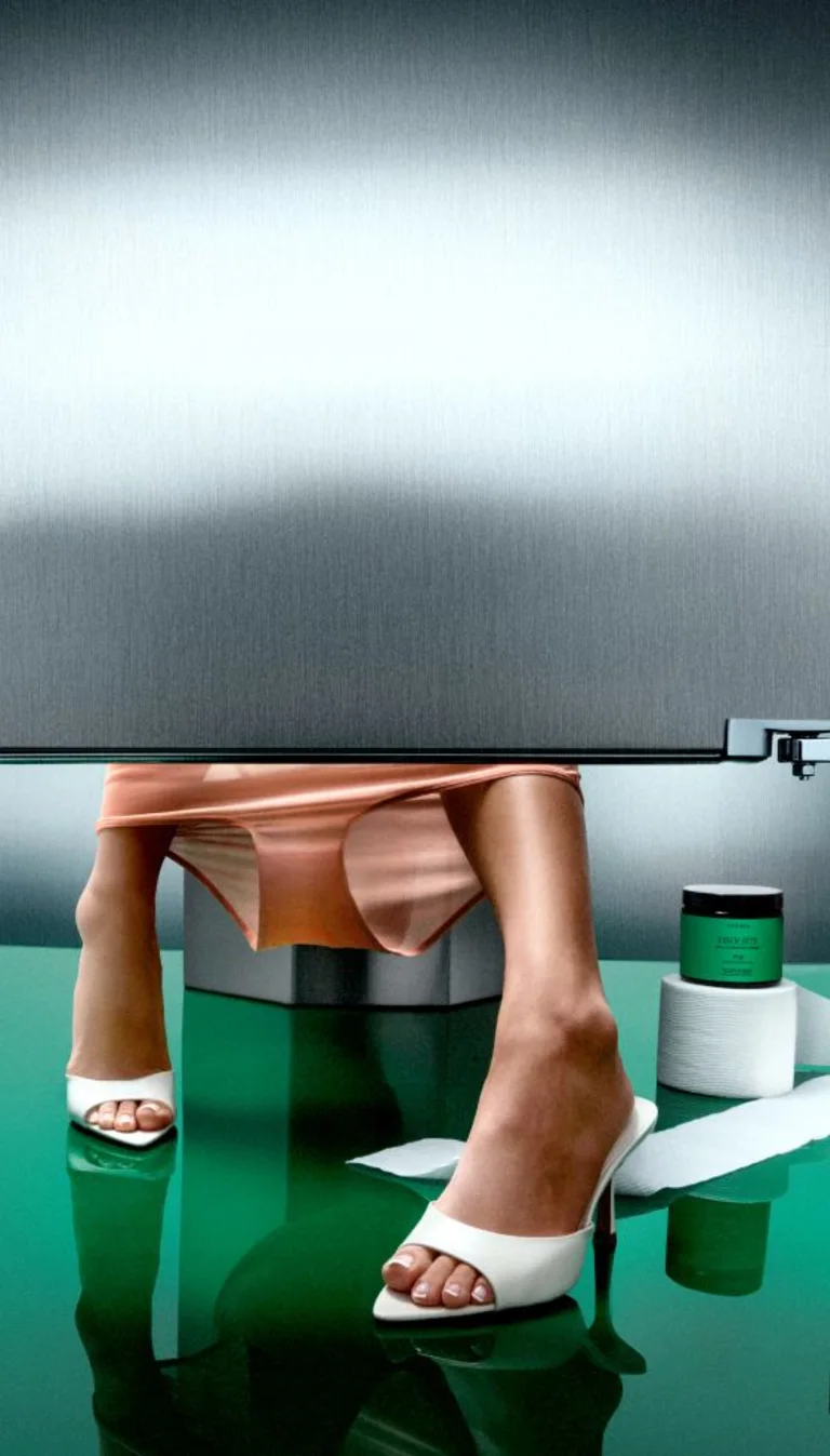 Woman in heels sitting on toilet behind a bathroom stall with fiber bite next to her.