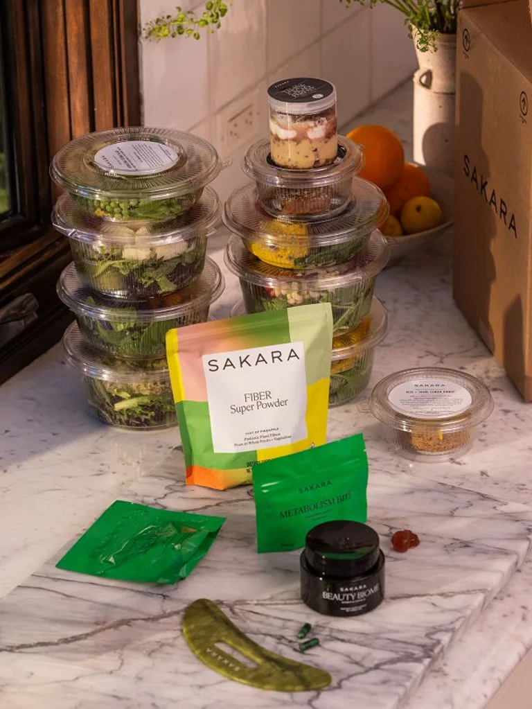 Sakara salads in plastic container sitting on counter with Fiber Powder, Metabolism Bite and Beauty Biome in front 