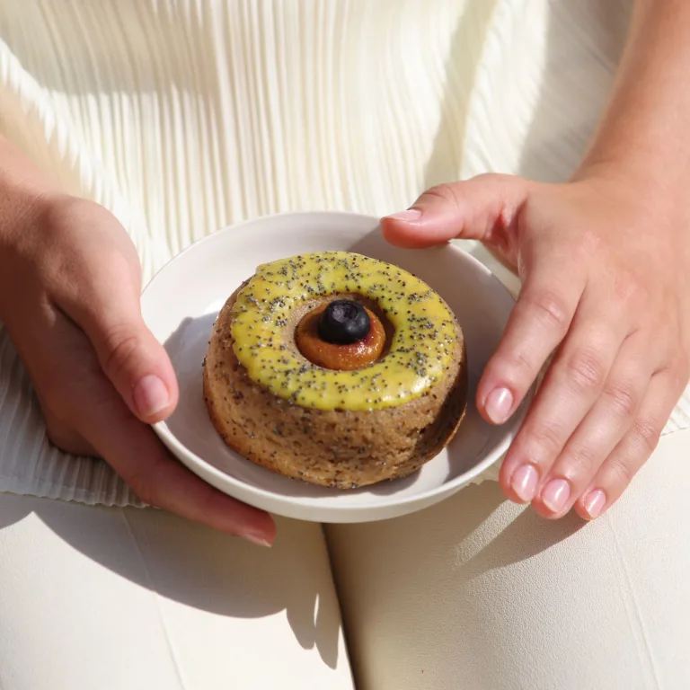 Woman in cream clothing holding donut with yellow frosting